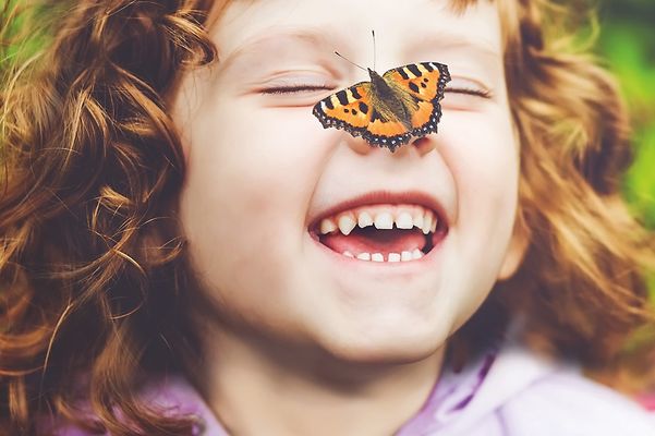 Schwarz-orange gemusterter Schmetterling landet auf der Nase eines kleinen Mädchens, welches lacht.
