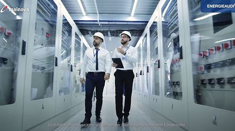 © Mainova AG Zwei Männer in weißen Hemden und Helmen gehen durch einen Korridor mit technischen Geräten.