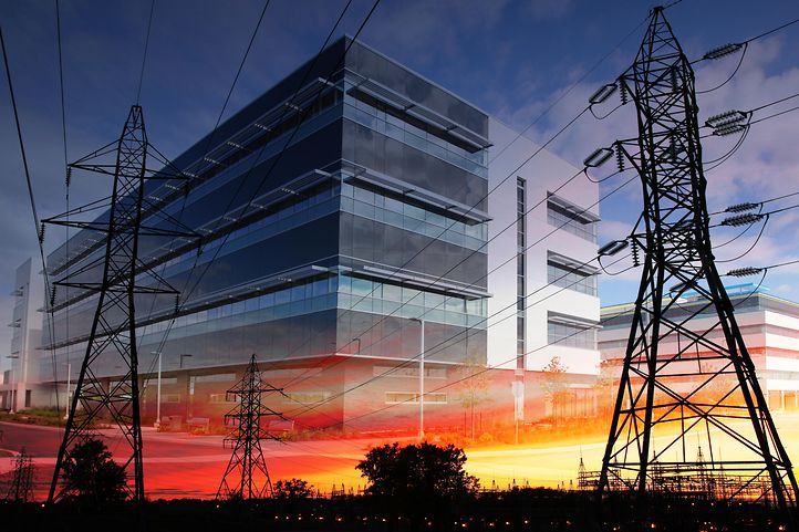 Ein modernes Bürogebäude mit Glasfassade und Strommasten im Vordergrund bei Sonnenuntergang.