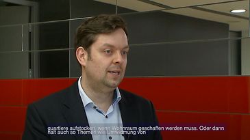 Ein Mann in einem Anzug steht vor einer Wand mit roten und grauen Paneelen