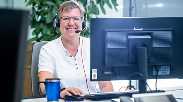 Eine Person mit Kopfhörern sitzt vor einem Computerbildschirm in einem Büro.