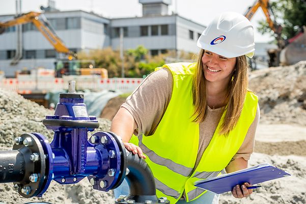 Frau mit Helm und Warnweste prüft eine Pumpe auf einer Baustelle