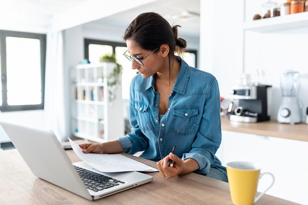 Junge Frau sitzt zu Hause vor ihrem Laptop und füllt einen Antrag aus.