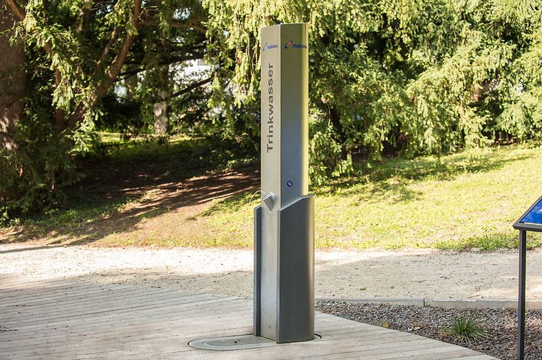 Eine Trinkwasserstation im Freien, umgeben von Bäumen und einem Weg.