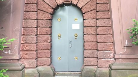 Eine graue Tür mit goldenen Verzierungen in einem roten Backsteingebäude.