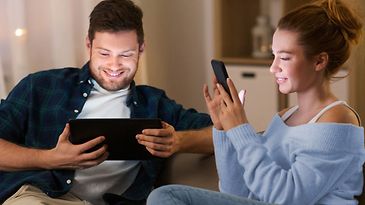 Paar sitzt mit Smartphone und Tablet auf Sofa