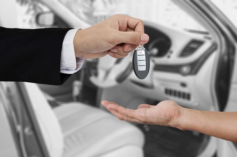 Ein Autoschlüssel wird von einer Hand zur anderen Hand übergeben.