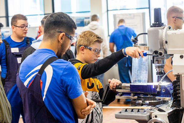 Eine Gruppe von Menschen beobachtet einen Jungen, der an einer Fräsmaschine arbeitet.