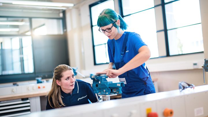 Ausbilderin kontrolliert die Arbeit einer Auszubildenden an einen Schraubstock 