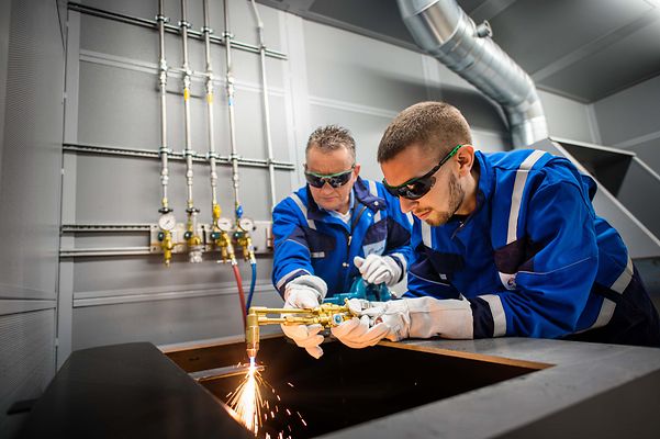 Ausbilder hilft Auszubildenden bei Schweißarbeiten