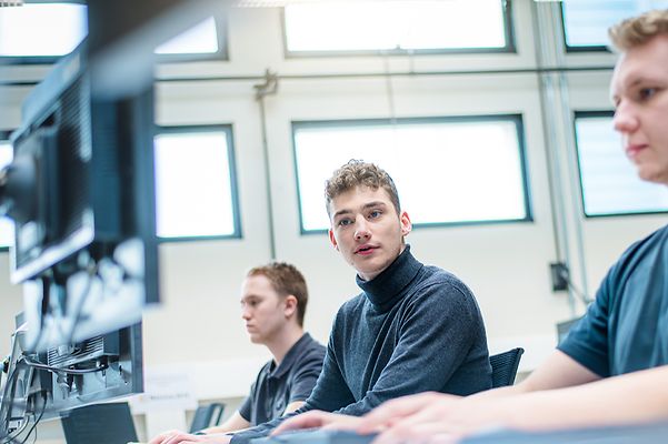 Auszubildende sitzen alle am Computer und ein Auszubildender schaut auf dem Monitor des anderen
