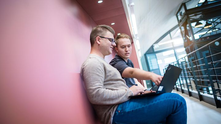 Ausbilder sitzt mit Notebook und bekommt vom Auszubildenden etwas am Monitor gezeigt