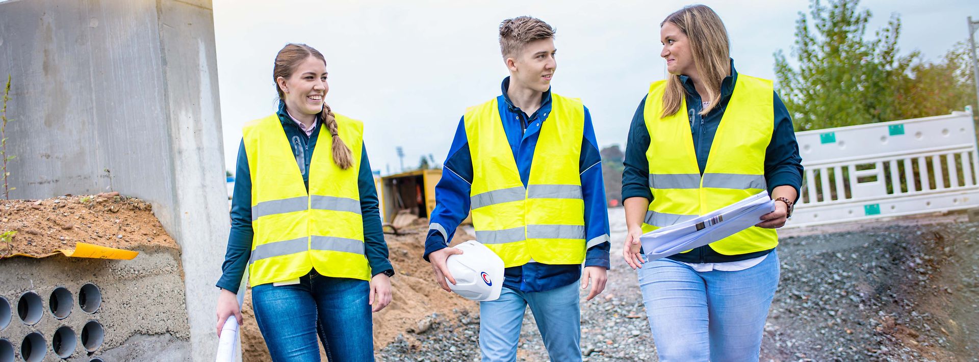 Gruppe Auszubildender läuft durch eine Baustelle und sprechen miteinander