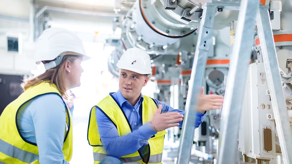 Ausbilder erklärt einer Auszubildenden eine Maschine