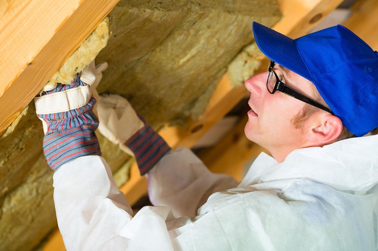 Ein Mann in Arbeitskleidung befestigt Dämmwolle zwischen Dachsparren