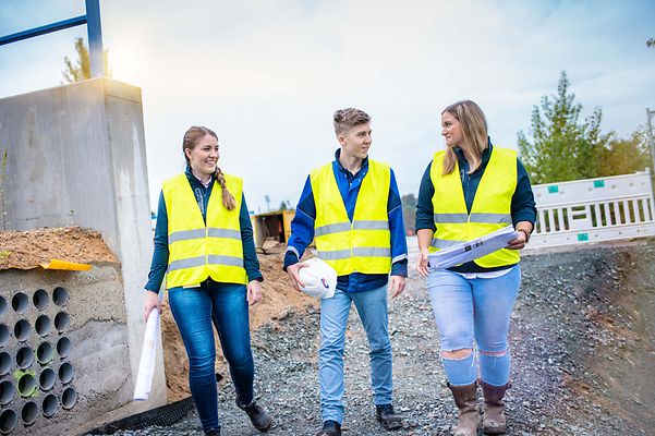 Gruppe Auszubildender läuft ducrh eine Baustelle und sprechen miteinander