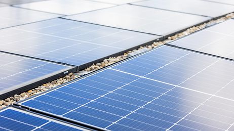 Mehrere blaue Solarpaneele auf einem Kiesdach, in Reihen angeordnet, mit gitterförmiger Zellstruktur.