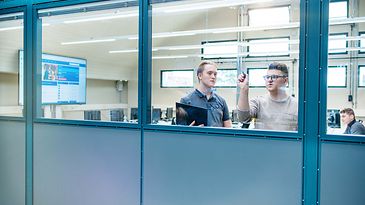 Zwei Auszubildende schreiben im Seminarraum etwas an die Scheibe. Fotografiert von Außen.